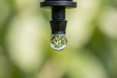 Gros plan macro d'une goutte d'eau perlant d'un tuyau d'irrigation noir